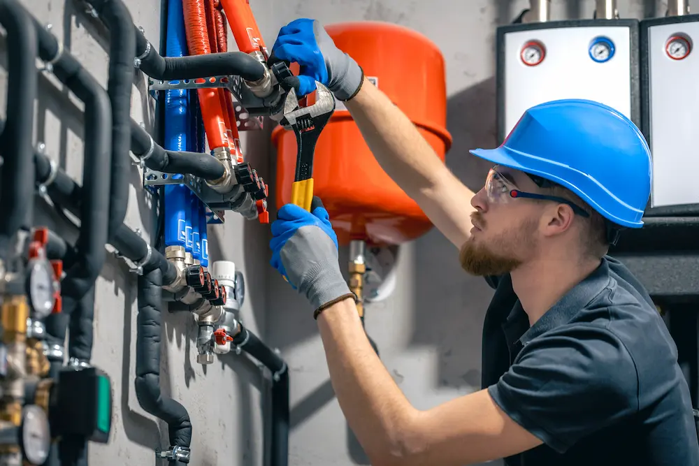 Operário com luvas, óculos de proteção e capacete realizando manutenção de sistemas de refrigeração com chave inglesa