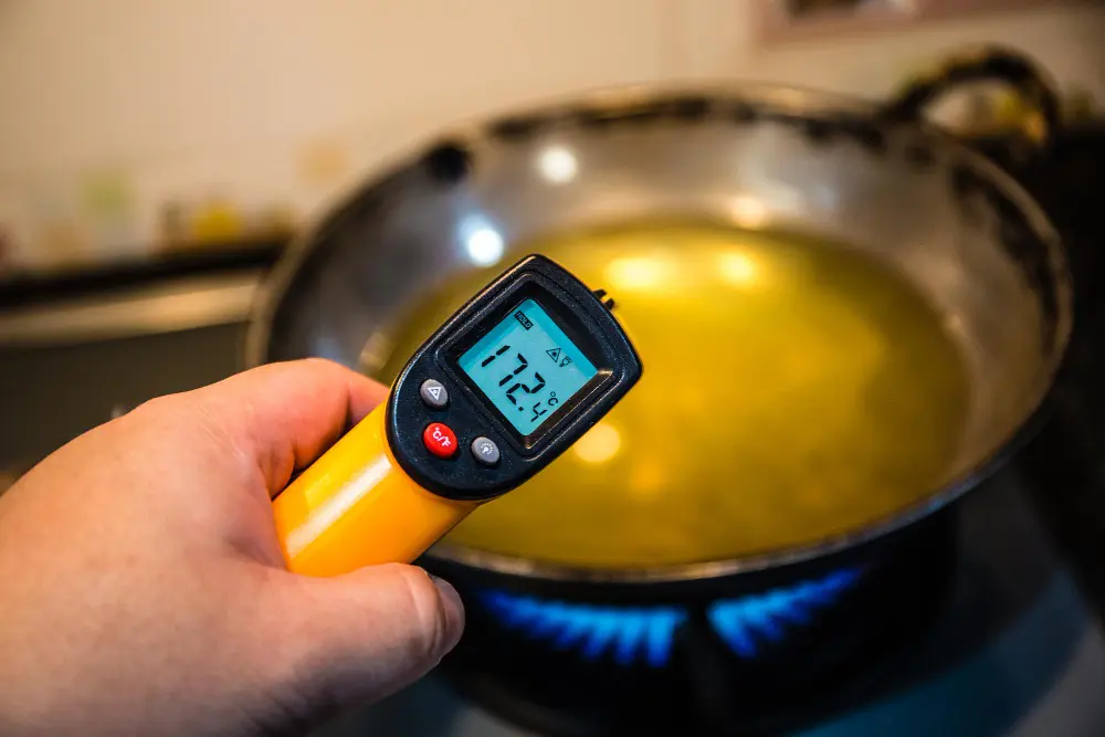Mão segurando termômetro digital em cima de panela com óleo para  controle de temperatura dos alimentos